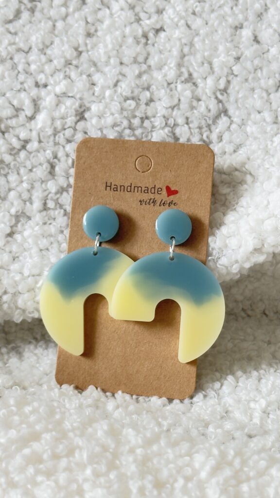 Paire de boucles d'oreilles en résine époxy en forme de 3/4 de rond surmontées d'un rond au niveau de l'attache, attachées à un carton fait main