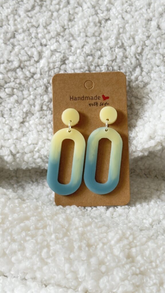 Paire de boucles d'oreilles en résine époxy en forme d'ovale creux surmontées d'un rond au niveau de l'attache, attachées à un carton fait main