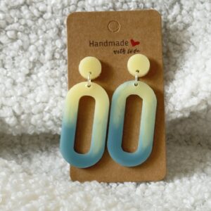 Paire de boucles d'oreilles en résine époxy en forme d'ovale creux surmontées d'un rond au niveau de l'attache, attachées à un carton fait main