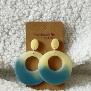 Paire de boucles d'oreilles en résine époxy en forme ronds creux surmontés d'un ovale au niveau de l'attache, attachées à un carton fait main