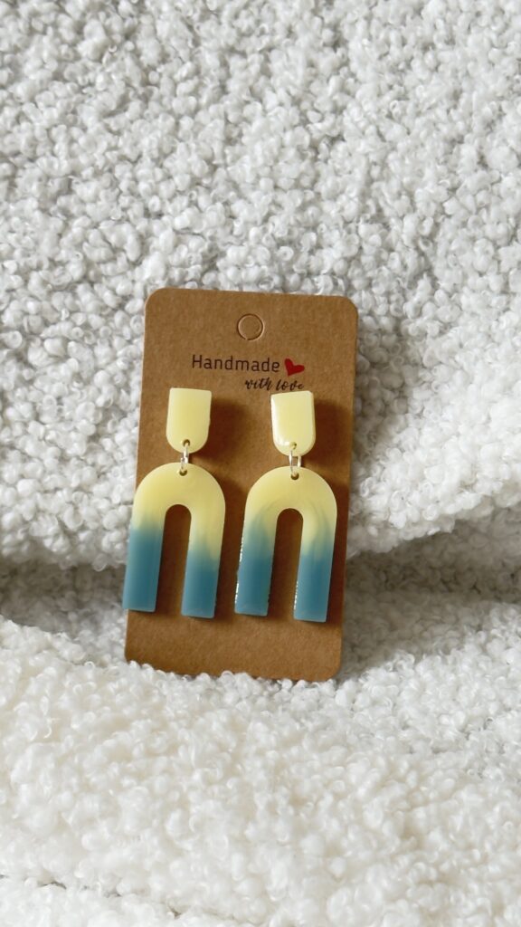 Paire de boucles d'oreilles en résine époxy en forme de "U" creux surmontées d'un "U" plein au niveau de l'attache, attachées à un carton fait main