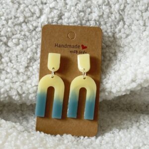 Paire de boucles d'oreilles en résine époxy en forme de "U" creux surmontées d'un "U" plein au niveau de l'attache, attachées à un carton fait main