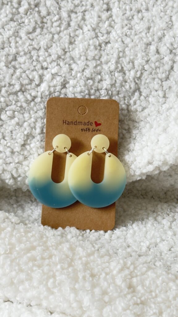 Paire de boucles d'oreilles en résine époxy en forme de Pacman inversé surmontées d'un rond au niveau de l'attache, attachées à un carton fait main