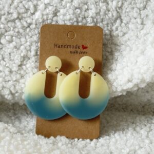 Paire de boucles d'oreilles en résine époxy en forme de Pacman inversé surmontées d'un rond au niveau de l'attache, attachées à un carton fait main