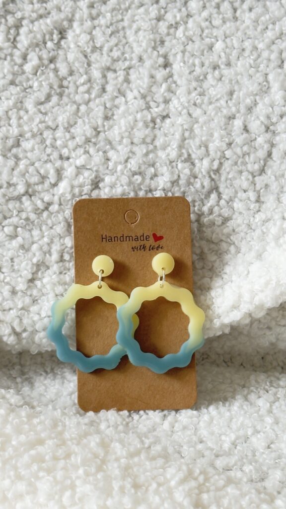 Paire de boucles d'oreilles en résine époxy en forme de vagues rondes surmontées d'un rond au niveau de l'attache, attachées à un carton fait main
