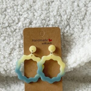 Paire de boucles d'oreilles en résine époxy en forme de vagues rondes surmontées d'un rond au niveau de l'attache, attachées à un carton fait main