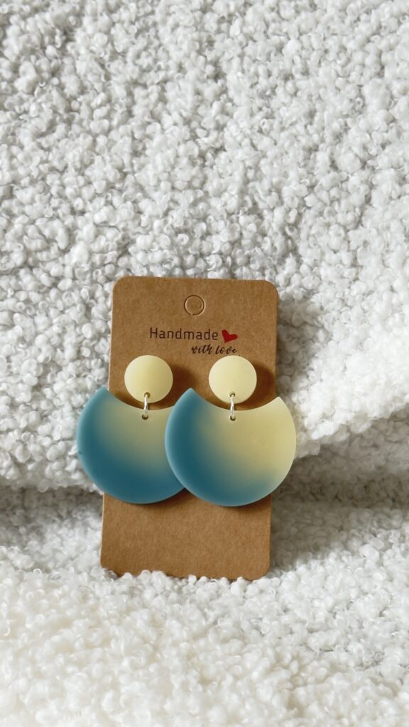Paire de boucles d'oreilles en résine époxy en forme de grande demi-lune, surmontée d'un rond au niveau de l'attache, attachées à un carton fait main