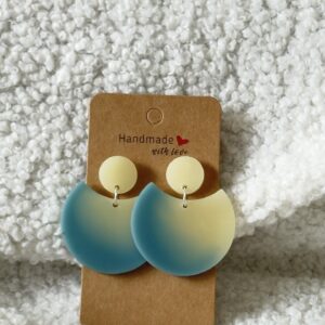 Paire de boucles d'oreilles en résine époxy en forme de grande demi-lune, surmontée d'un rond au niveau de l'attache, attachées à un carton fait main