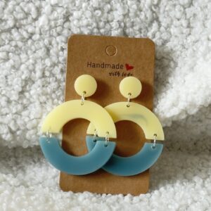Paire de boucles d'oreilles en résine époxy en forme de deux demi-cercles attachés et surmontés d'un rond au niveau de l'attache, attachées à un carton fait main