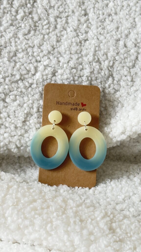 Paire de boucles d'oreilles en résine époxy en forme d'oval creux surmonté d'un rond au niveau de l'attache attachées à un carton fait main