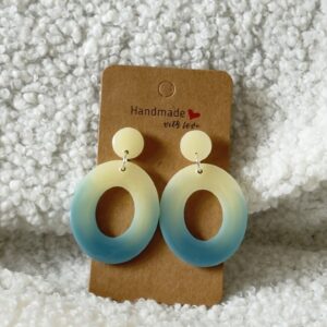 Paire de boucles d'oreilles en résine époxy en forme d'oval creux surmonté d'un rond au niveau de l'attache attachées à un carton fait main
