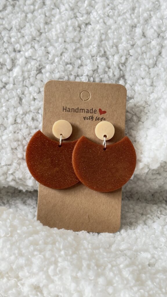 Paire de boucles d'oreilles en résine époxy en forme de grande demi-lune, surmontée d'un rond au niveau de l'attache, attachées à un carton fait main