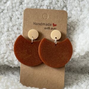 Paire de boucles d'oreilles en résine époxy en forme de grande demi-lune, surmontée d'un rond au niveau de l'attache, attachées à un carton fait main