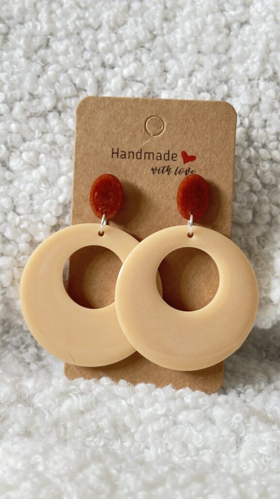 Paire de boucles d'oreilles en résine époxy en forme ronds creux surmontés d'un rond au niveau de l'attache, attachées à un carton fait main