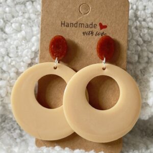 Paire de boucles d'oreilles en résine époxy en forme ronds creux surmontés d'un rond au niveau de l'attache, attachées à un carton fait main