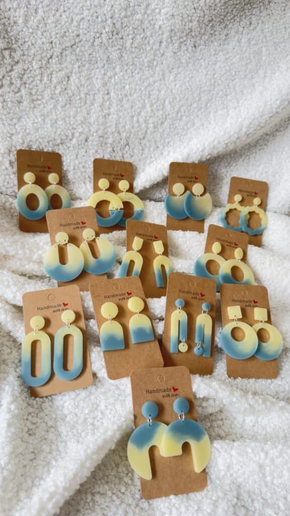 Collection de boucles d'oreilles en résine époxy bicolores jaune et bleu mer en forme d'oval creux surmonté d'un rond au niveau de l'attache attachées à un carton fait main