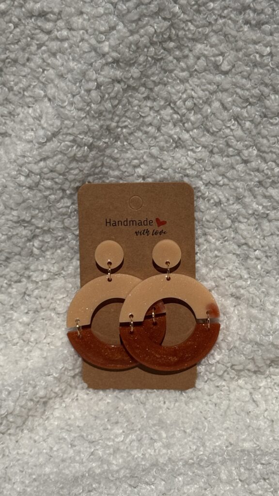 Paire de boucles d'oreilles en résine époxy en forme de deux demi-cercles attachés et surmontés d'un rond au niveau de l'attache, attachées à un carton fait main