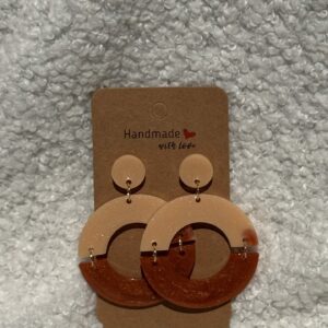Paire de boucles d'oreilles en résine époxy en forme de deux demi-cercles attachés et surmontés d'un rond au niveau de l'attache, attachées à un carton fait main