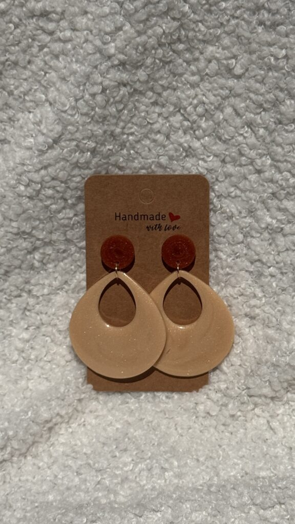 Paire de boucles d'oreilles en résine époxy en forme de goutte creuse surmontées d'un rond au niveau de l'attache, attachées à un carton fait main