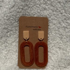 Paire de boucles d'oreilles en résine époxy en forme d'ovale creux surmontées d'un rond au niveau de l'attache, attachées à un carton fait main