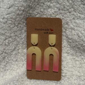 Paire de boucles d'oreilles en résine époxy en forme de "U" creux surmontées d'un "U" plein au niveau de l'attache, attachées à un carton fait main