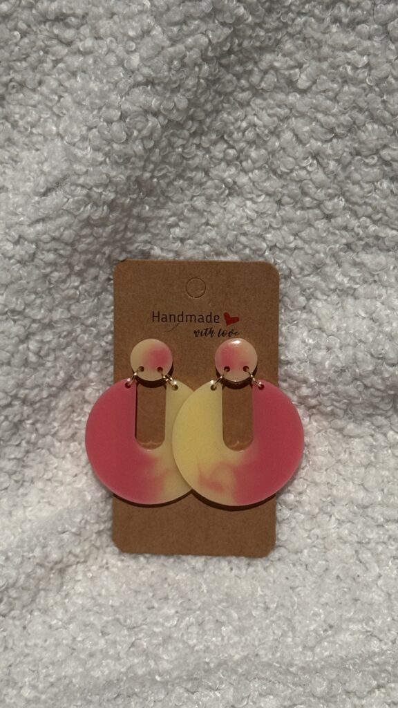 Paire de boucles d'oreilles en résine époxy en forme de Pacman inversé surmontées d'un rond au niveau de l'attache, attachées à un carton fait main
