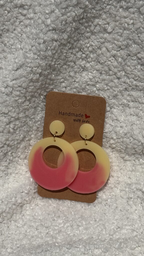 Paire de boucles d'oreilles en résine époxy en forme ronds creux surmontés d'un ovale au niveau de l'attache, attachées à un carton fait main