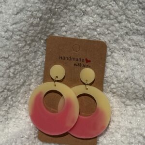 Paire de boucles d'oreilles en résine époxy en forme ronds creux surmontés d'un ovale au niveau de l'attache, attachées à un carton fait main