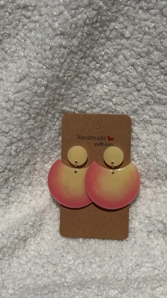 Paire de boucles d'oreilles en résine époxy en forme de grande demi-lune, surmontée d'un rond au niveau de l'attache, attachées à un carton fait main