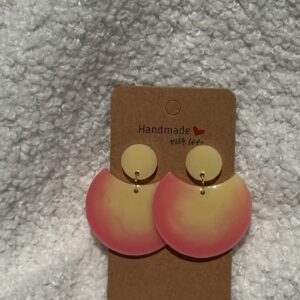 Paire de boucles d'oreilles en résine époxy en forme de grande demi-lune, surmontée d'un rond au niveau de l'attache, attachées à un carton fait main