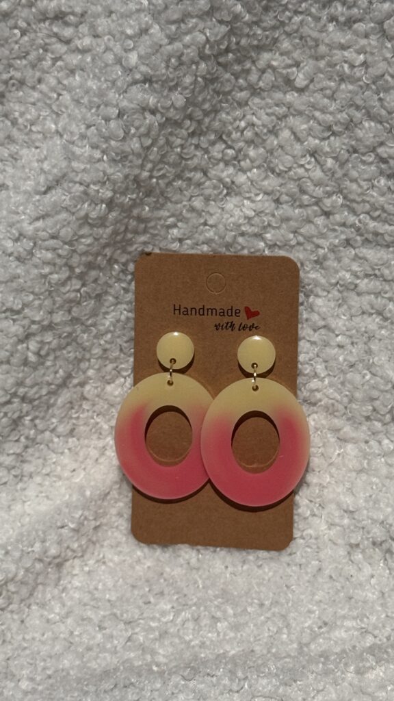 Paire de boucles d'oreilles en résine époxy en forme d'oval creux surmonté d'un rond au niveau de l'attache attachées à un carton fait main