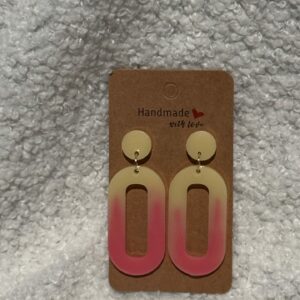 Paire de boucles d'oreilles en résine époxy en forme d'ovale creux surmontées d'un rond au niveau de l'attache, attachées à un carton fait main