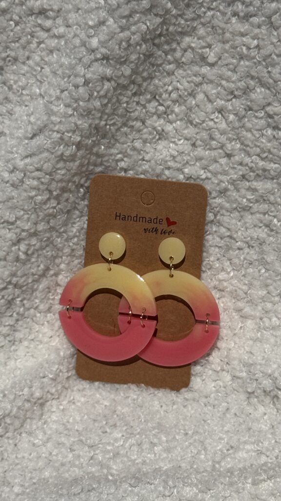 Paire de boucles d'oreilles en résine époxy en forme de deux demi-cercles attachés et surmontés d'un rond au niveau de l'attache, attachées à un carton fait main