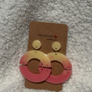 Paire de boucles d'oreilles en résine époxy en forme de deux demi-cercles attachés et surmontés d'un rond au niveau de l'attache, attachées à un carton fait main