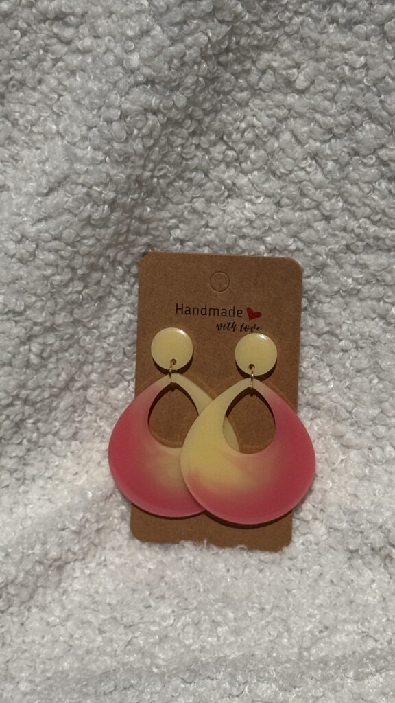 Paire de boucles d'oreilles en résine époxy en forme de goutte creuse surmontées d'un rond au niveau de l'attache, attachées à un carton fait main