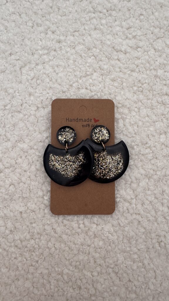 Paire de boucles d'oreilles en résine époxy en forme de grande demi-lune, surmontée d'un rond au niveau de l'attache, attachées à un carton fait main