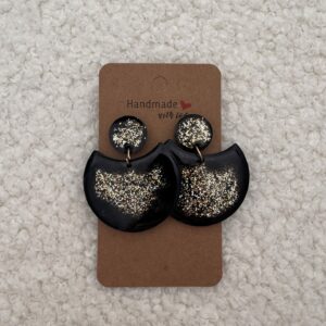 Paire de boucles d'oreilles en résine époxy en forme de grande demi-lune, surmontée d'un rond au niveau de l'attache, attachées à un carton fait main