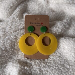 Boucles d'oreilles en résine époxy jaune givré, en forme de grand anneau rond creux, surmonté d'une puce ronde verte au niveau de l'attache. Attache en acier inoxydable.