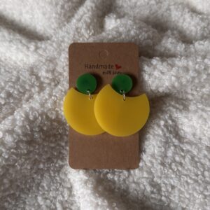 Boucles d'oreilles en résine époxy jaune givré, en forme de grande demi-lune arrondie, surmontée d'une puce ronde verte au niveau de l'attache. Attache en acier inoxydable.