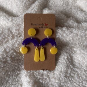 Boucles d'oreilles en résine époxy, arche violette surmontée d'une puce ronde jaune, agrémentée de deux pampilles jaunes (une boule et une goutte) en alternance sur chaque oreille. Attache en acier inoxydable.